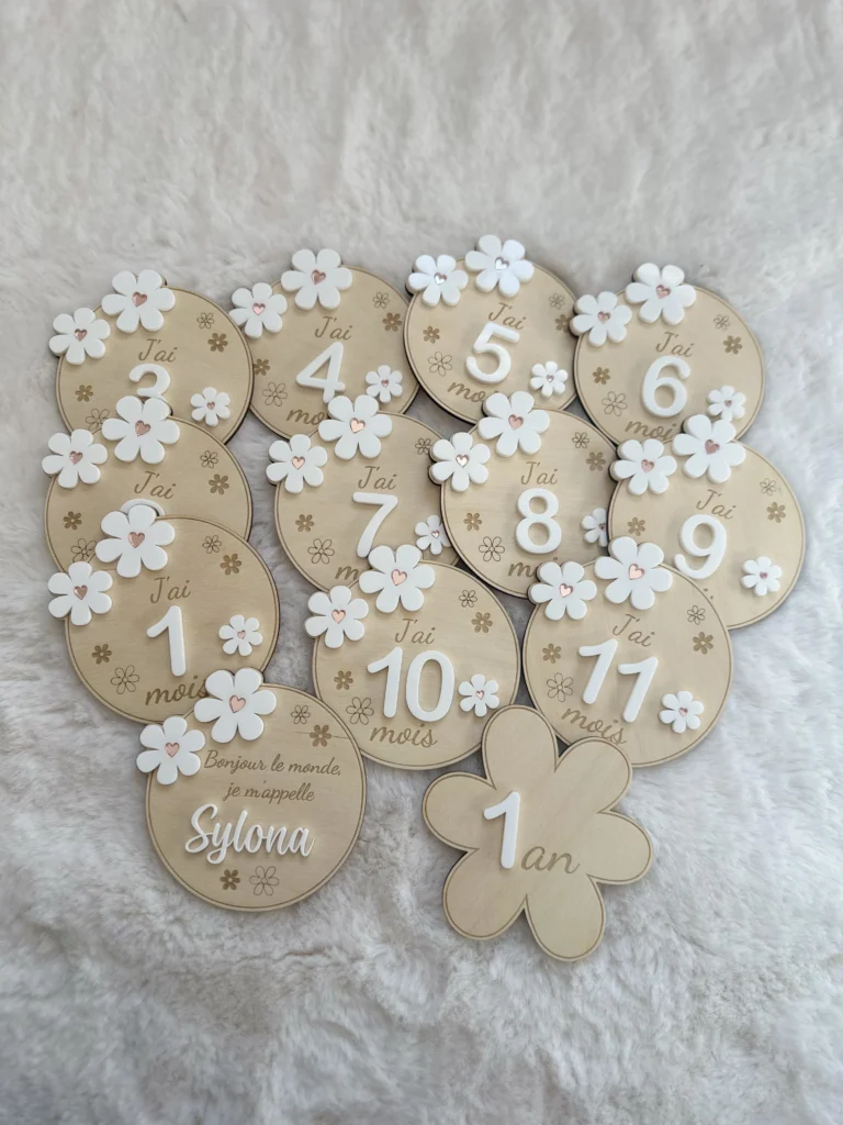 alt="Set de cartes étapes en bois personnalisées avec prénom, décorées de fleurs blanches en acrylique et chiffres en relief, pour marquer les premiers mois de bébé jusqu'à 1 an."